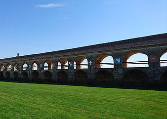 Historic stone arcade with medieval shields on green lawn