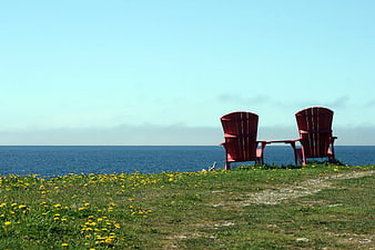 Red Adirondack Chairs Overlooking Ocean on Grassy Cliff