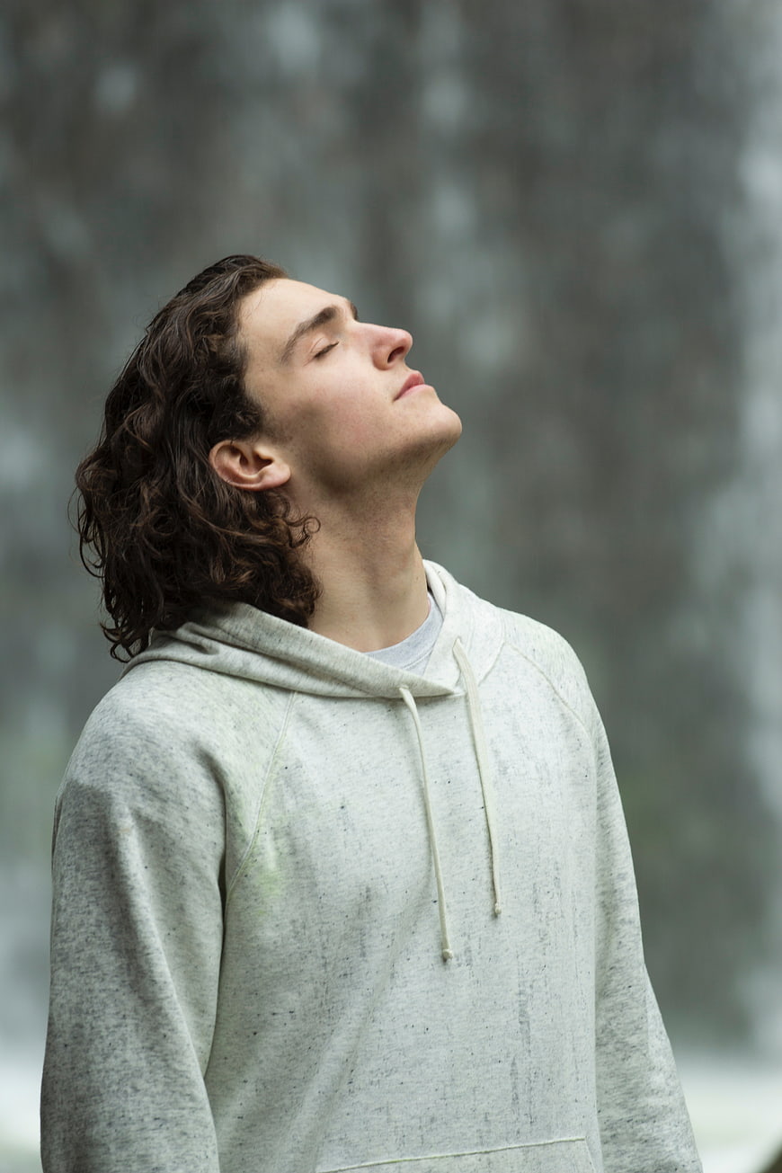 Young Man with Curly Hair Meditating in Hoodie