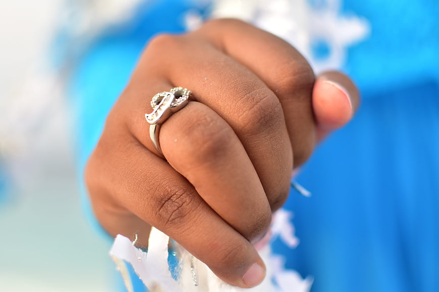 Close-up of hand wearing silver initial ring with blue background
