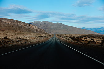 Endless asphalt road leading to mountains in arid landscape