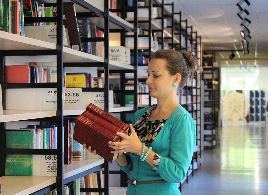 Woman holding red books in modern library aisle