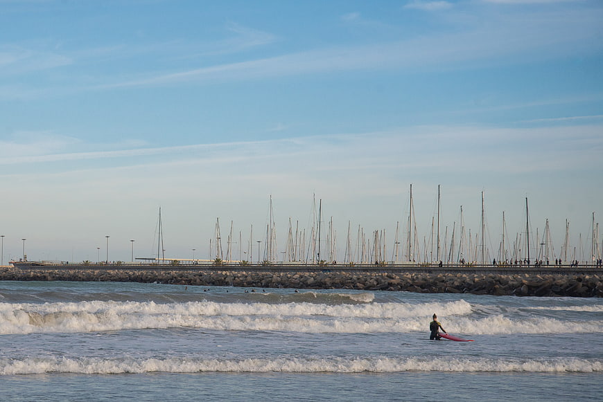 Surfer with red board walking in ocean waves near marina