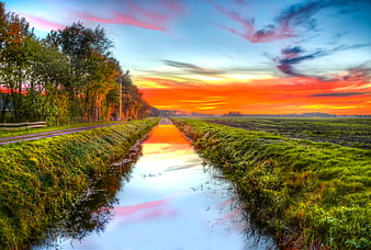 Vibrant sunset reflection in rural canal with green banks