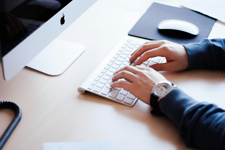 Hands Typing on White Keyboard at Modern Office Desk
