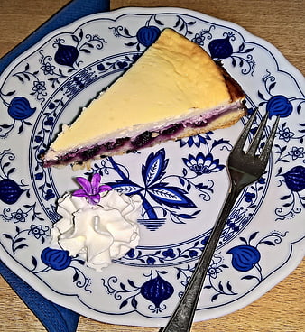 Slice of blueberry cheesecake with whipped cream on blue patterned plate