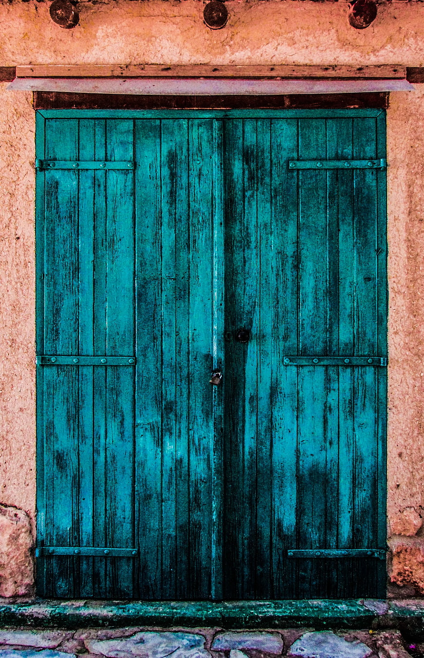 Weathered Teal Wooden Door on Textured Pink Wall