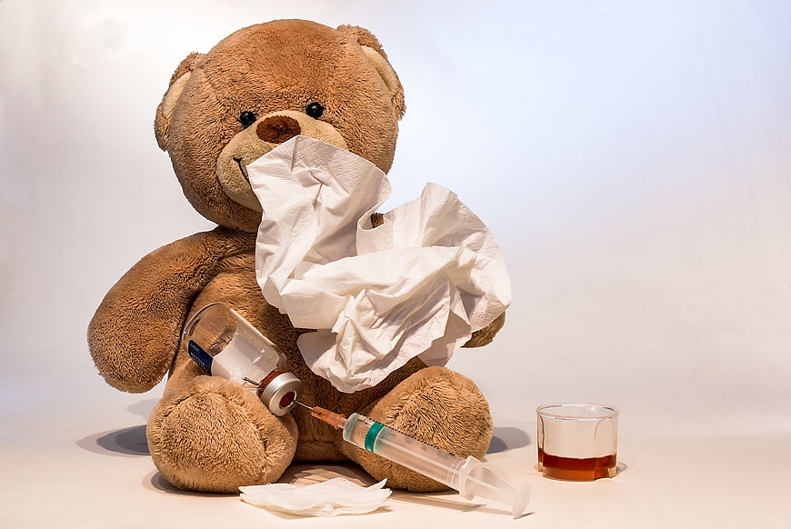 Sick teddy bear with tissues, syringe, and medicine