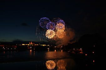 Colorful fireworks exploding over a river at night with city lights