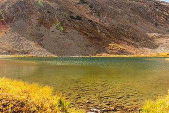 Alpine lake with golden autumn grass and rocky mountain backdrop