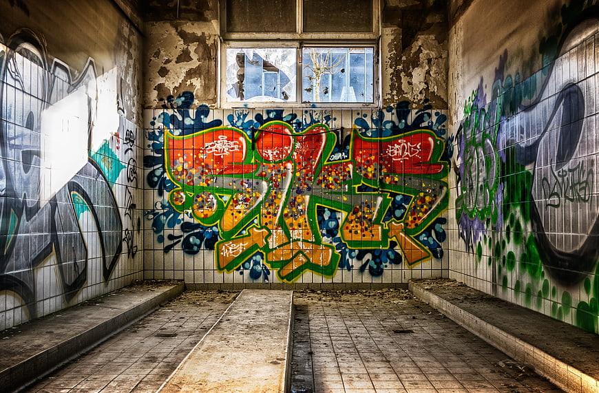 Abandoned tiled room with colorful graffiti and broken windows