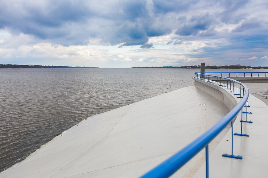 Curved Concrete Promenade with Blue Railing by the Sea
