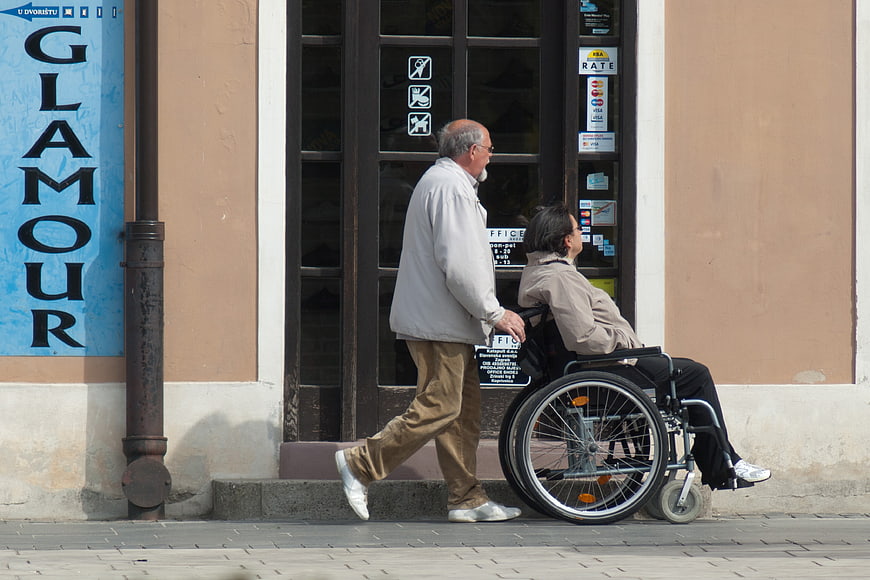 Senior man pushing woman in wheelchair on city street