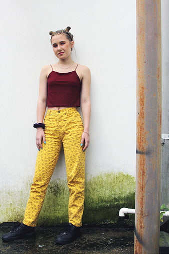Young woman in yellow patterned pants and maroon top posing outdoors
