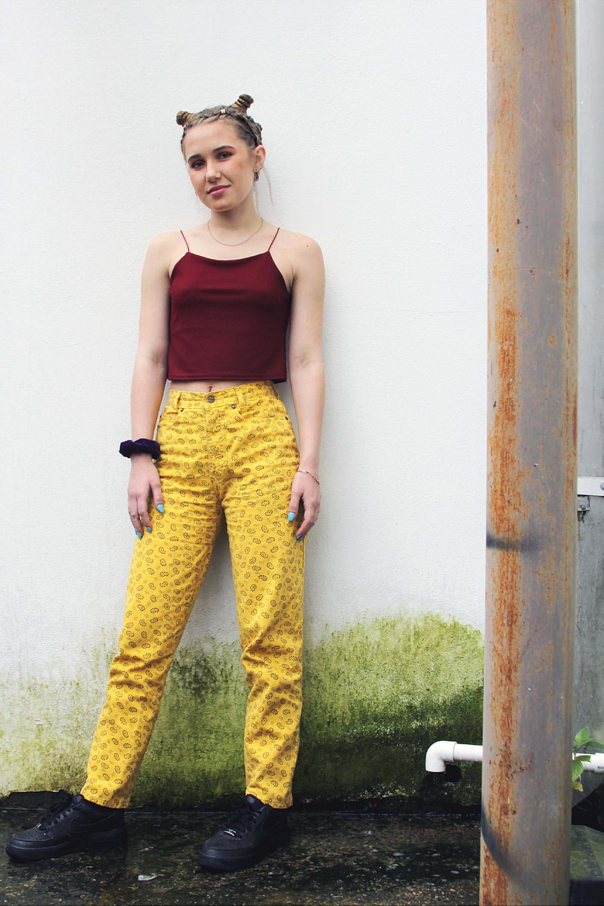 Young woman in yellow patterned pants and maroon top posing outdoors