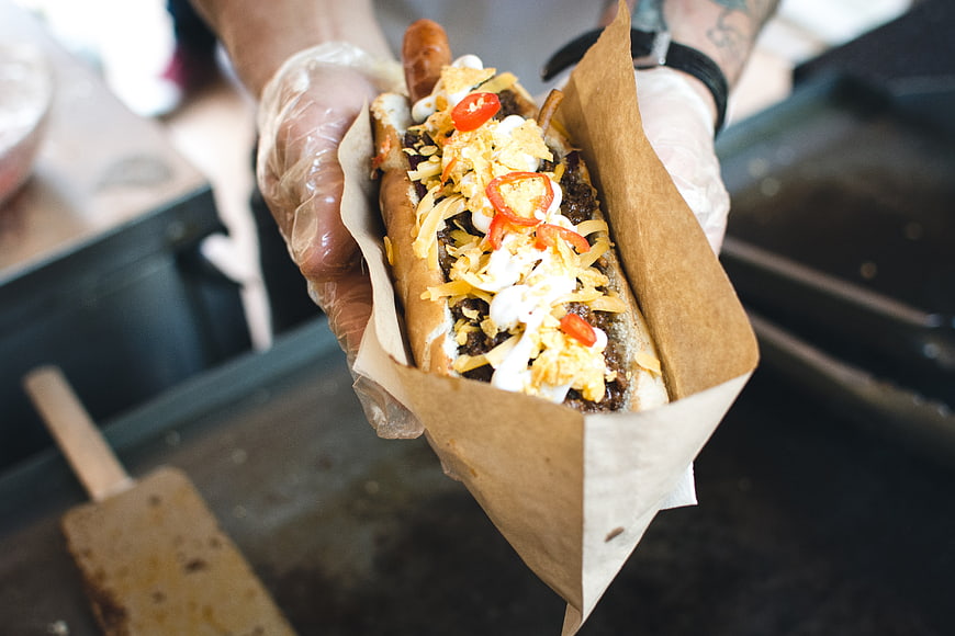 Loaded Gourmet Hot Dog Held in Hands