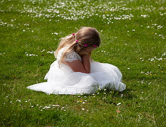 Sad little girl in white dress sitting in grassy field