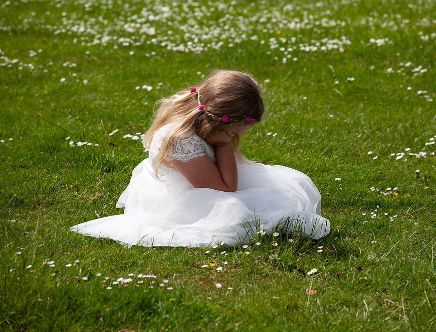 Sad little girl in white dress sitting in grassy field