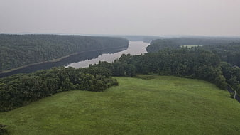 Aerial view of winding river through dense forest and green meadow