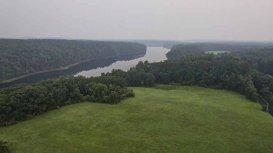 Aerial view of winding river through dense forest and green meadow