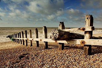 Weathered wooden groyne on pebble beach with dramatic sky