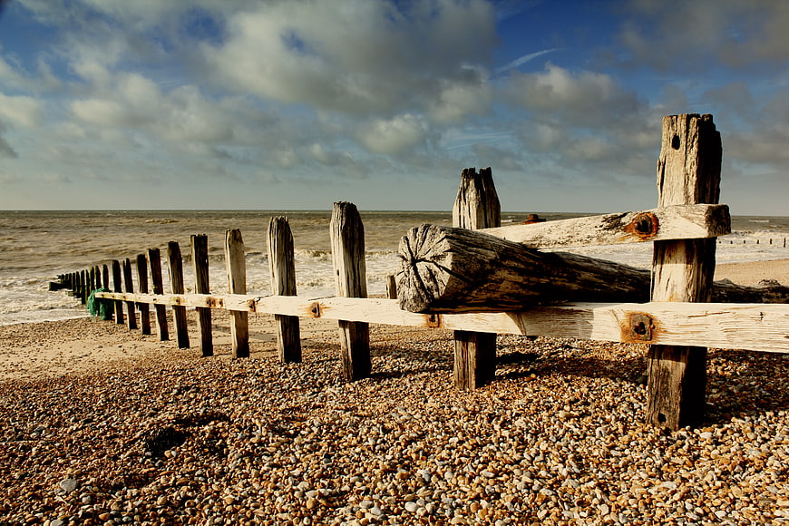 Weathered wooden groyne on pebble beach with dramatic sky