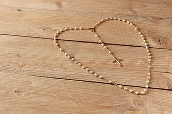 Gold rosary beads arranged in heart shape on wood