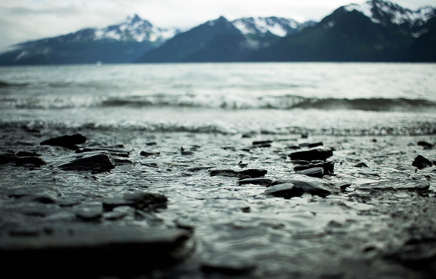 Low angle view of wet rocky shore with blurred mountains