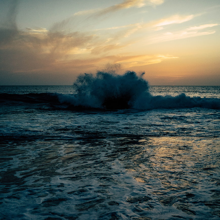 Dramatic Ocean Wave Crashing at Sunset with Golden Sky