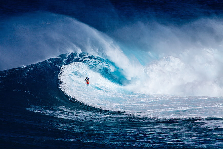 Surfer riding massive blue ocean wave barrel