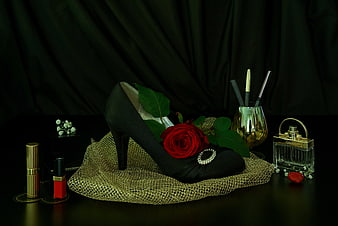 Elegant black high heel with red rose and gold cosmetics still life