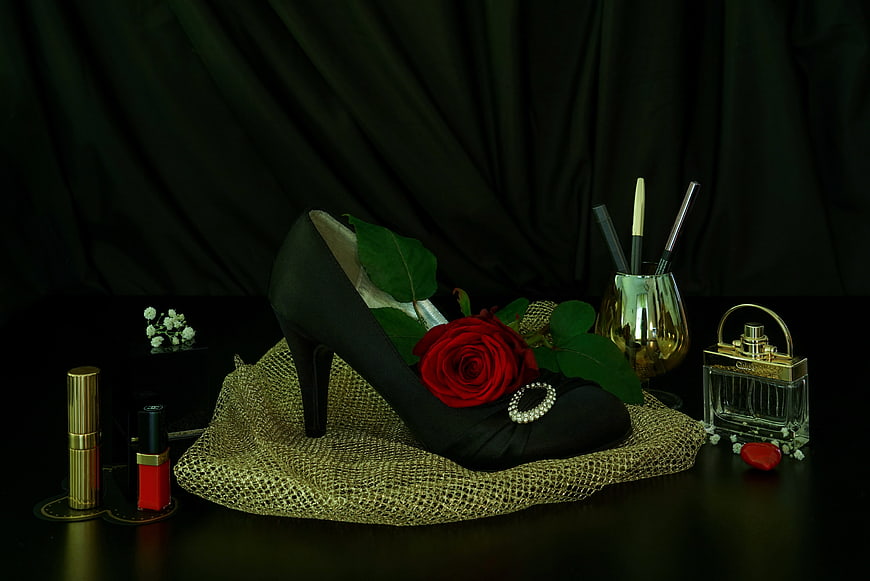 Elegant black high heel with red rose and gold cosmetics still life