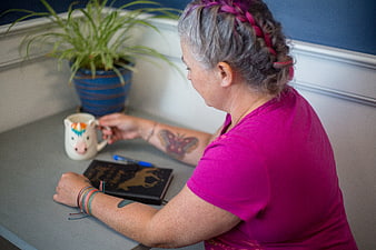 Senior woman with tattoos journaling at desk with unicorn mug
