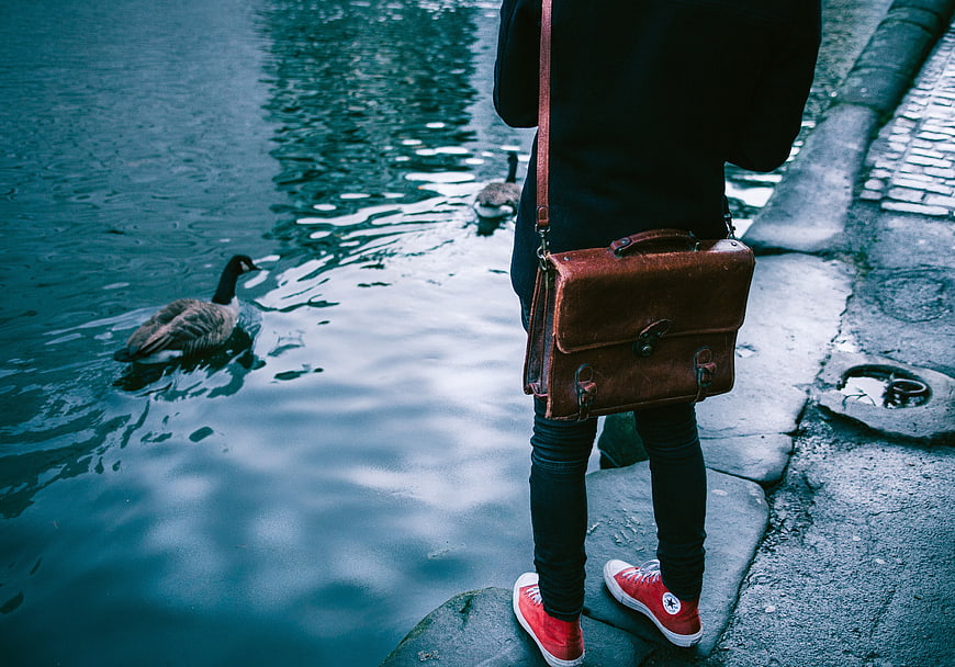 Person with brown leather bag and red sneakers by water