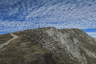 Lone Hiker on Mountain Ridge Under Cloudy Sky