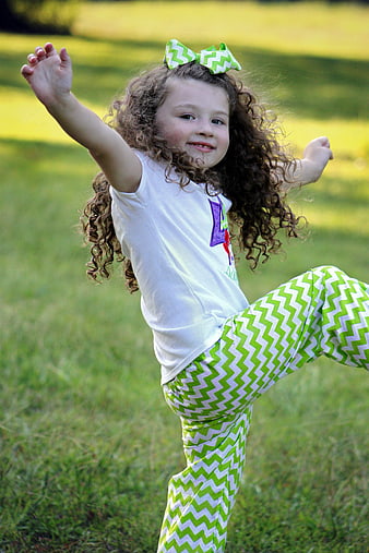 Happy curly-haired girl jumping in a green grassy field