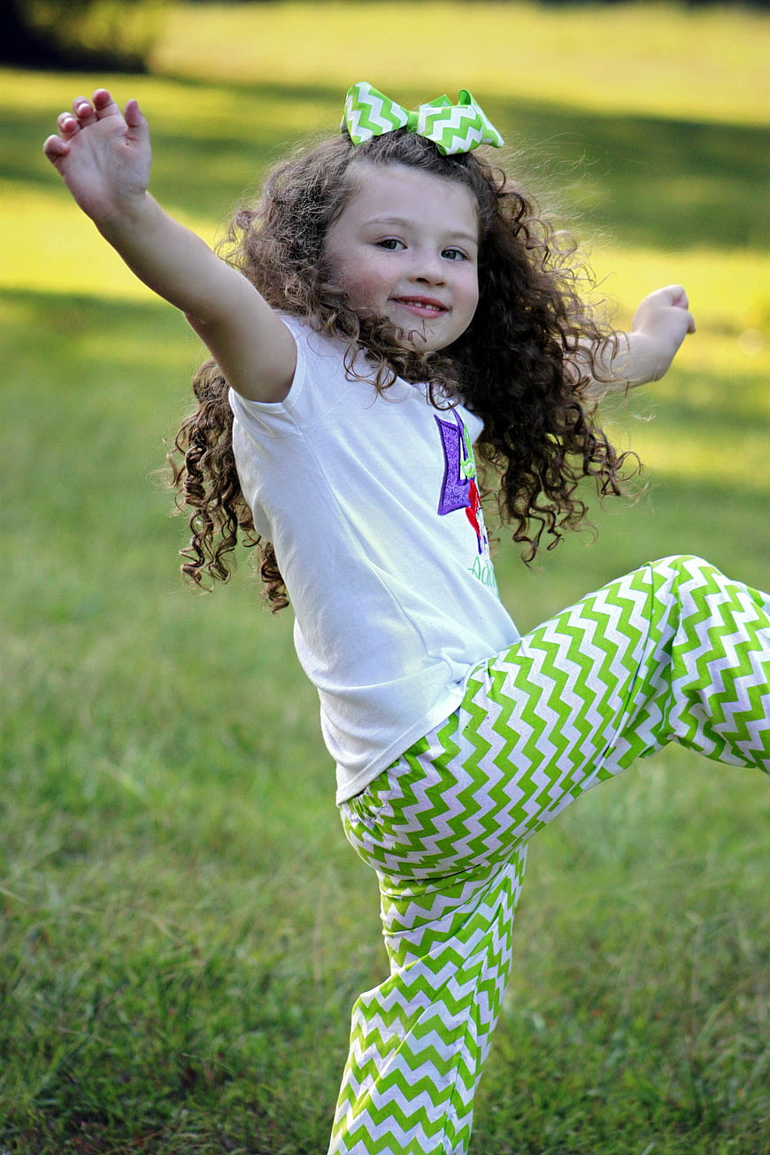 Happy curly-haired girl jumping in a green grassy field