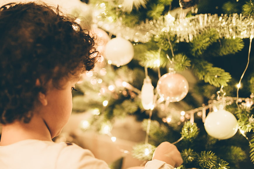 Child decorating Christmas tree with lights and ornaments