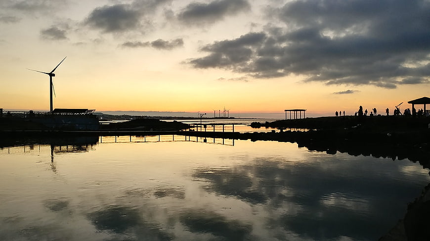 Silhouette of wind turbines and people at sunset by the sea