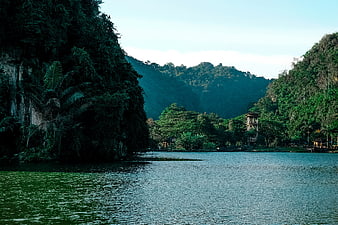 Serene tropical lake surrounded by lush green mountains and a traditional tower