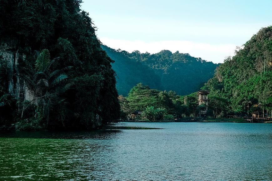 Serene tropical lake surrounded by lush green mountains and a traditional tower