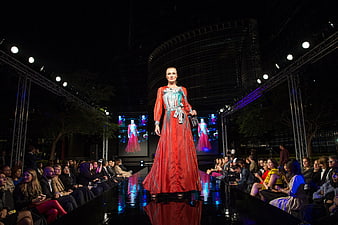 Female model walking the runway in a red gown at a night fashion show
