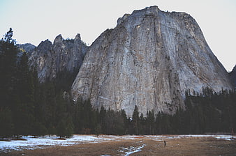 Majestic granite mountain peak with snow-dusted meadow and forest