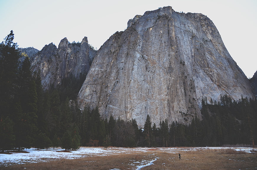 Majestic granite mountain peak with snow-dusted meadow and forest