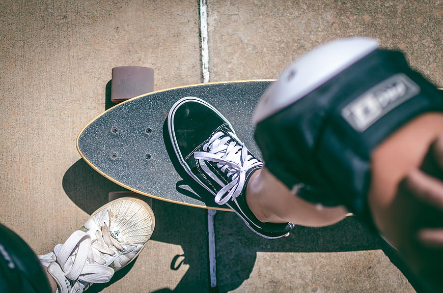 Top view of skateboarder feet on longboard with knee pads