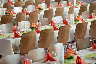 Rows of set banquet tables with orange napkins and wooden chairs