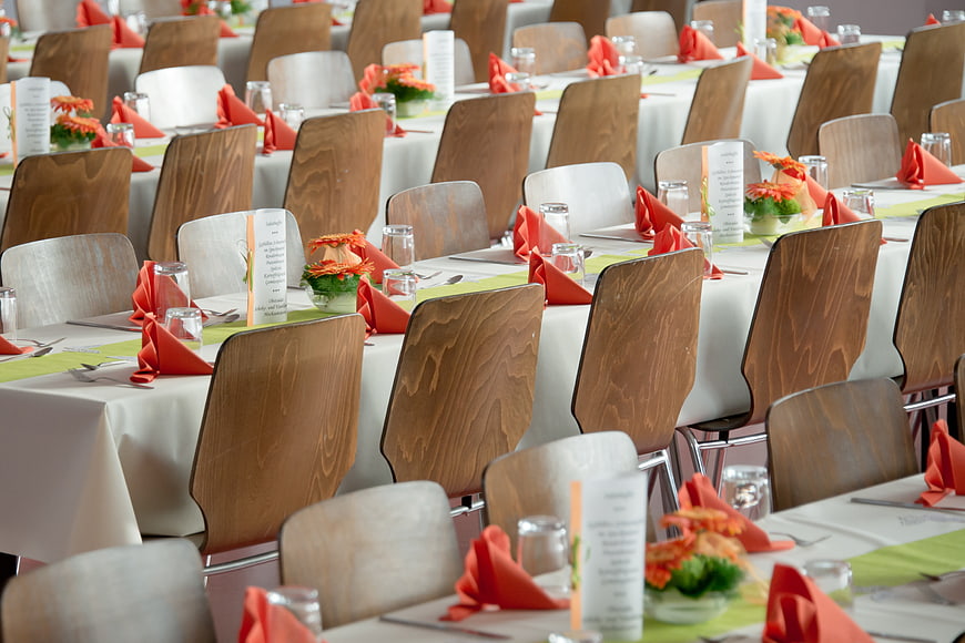Rows of set banquet tables with orange napkins and wooden chairs