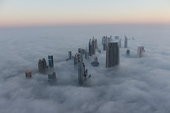 Aerial view of Dubai skyscrapers emerging from thick fog at sunrise