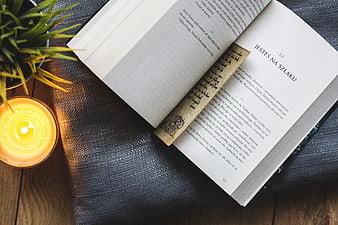 Open book with bookmark and candle on dark textured fabric