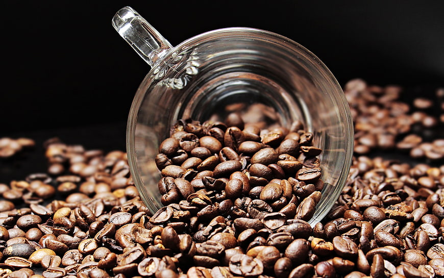 Roasted coffee beans spilling from a glass mug